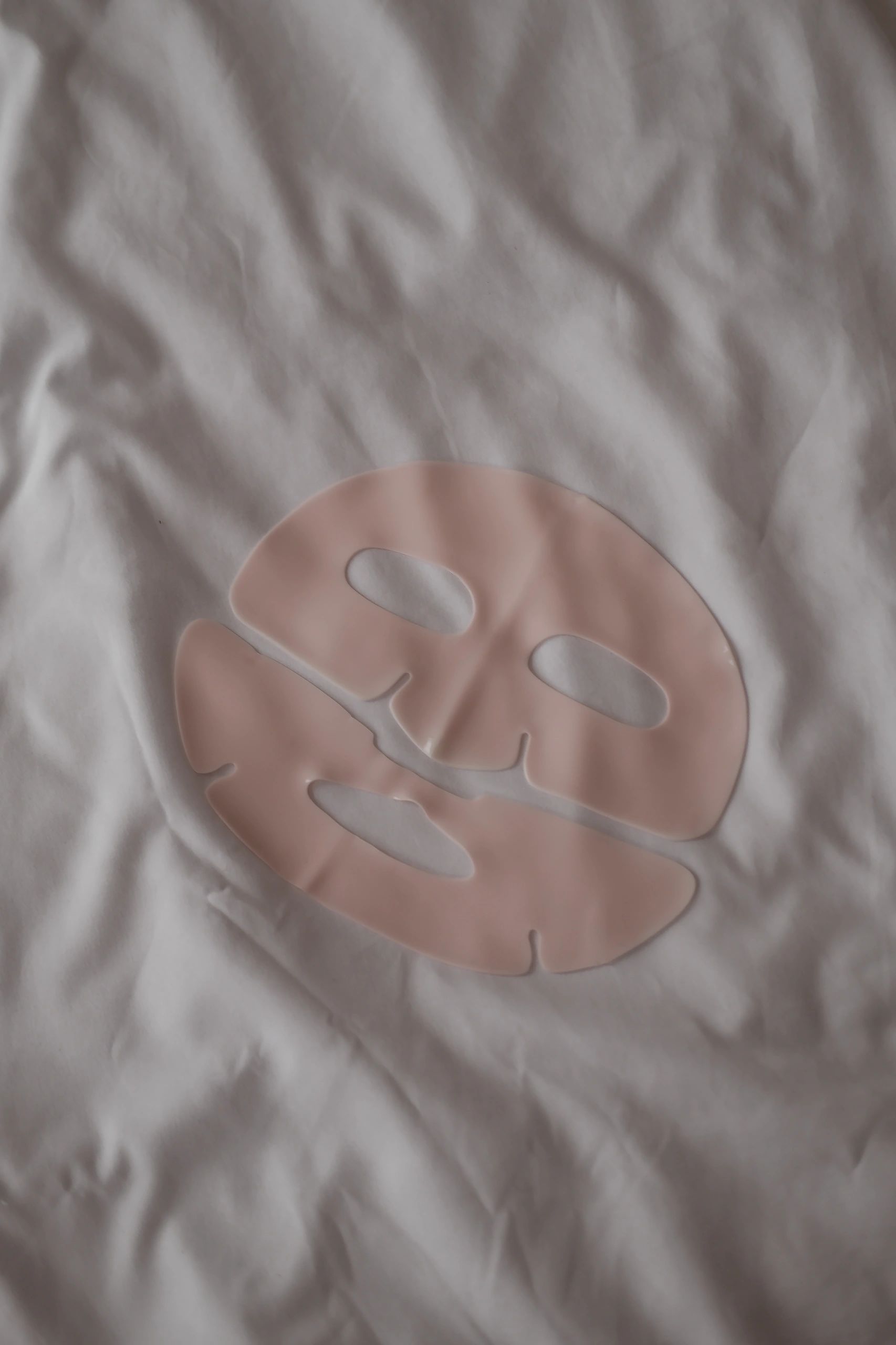 Light pink gel facial sheet mask on white beauty blogger flatlay